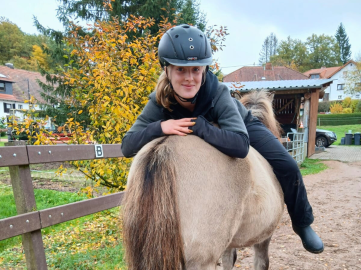 Junge Frau auf einem Islandpferd, freundlich lächelnd mit Reithelm, Symbolbild für Reitkurse und Veranstaltungen auf dem Gestüt Nahetal